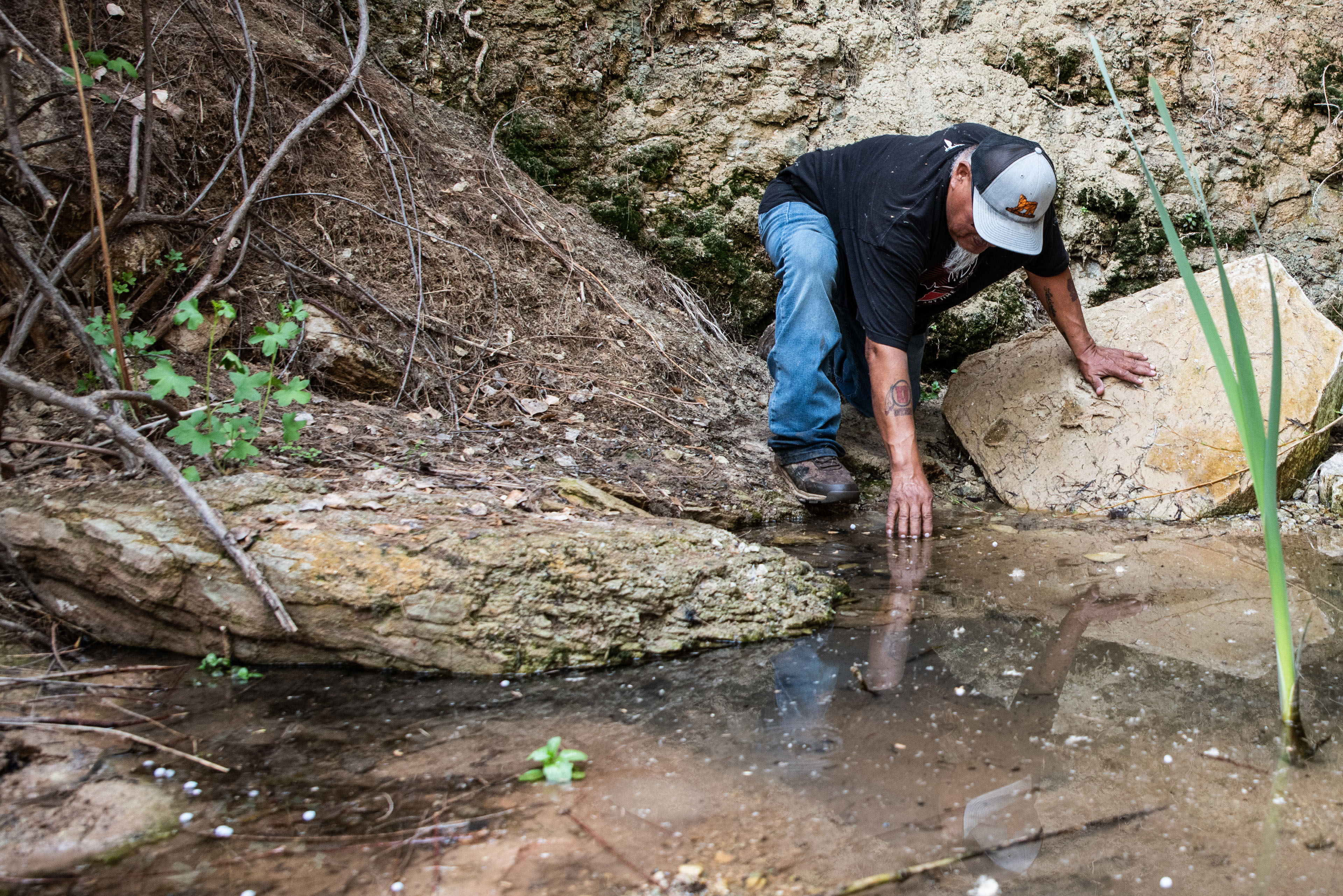 A photo of Malcolm Lehi reaching down to touch the water of Entrance Spring.