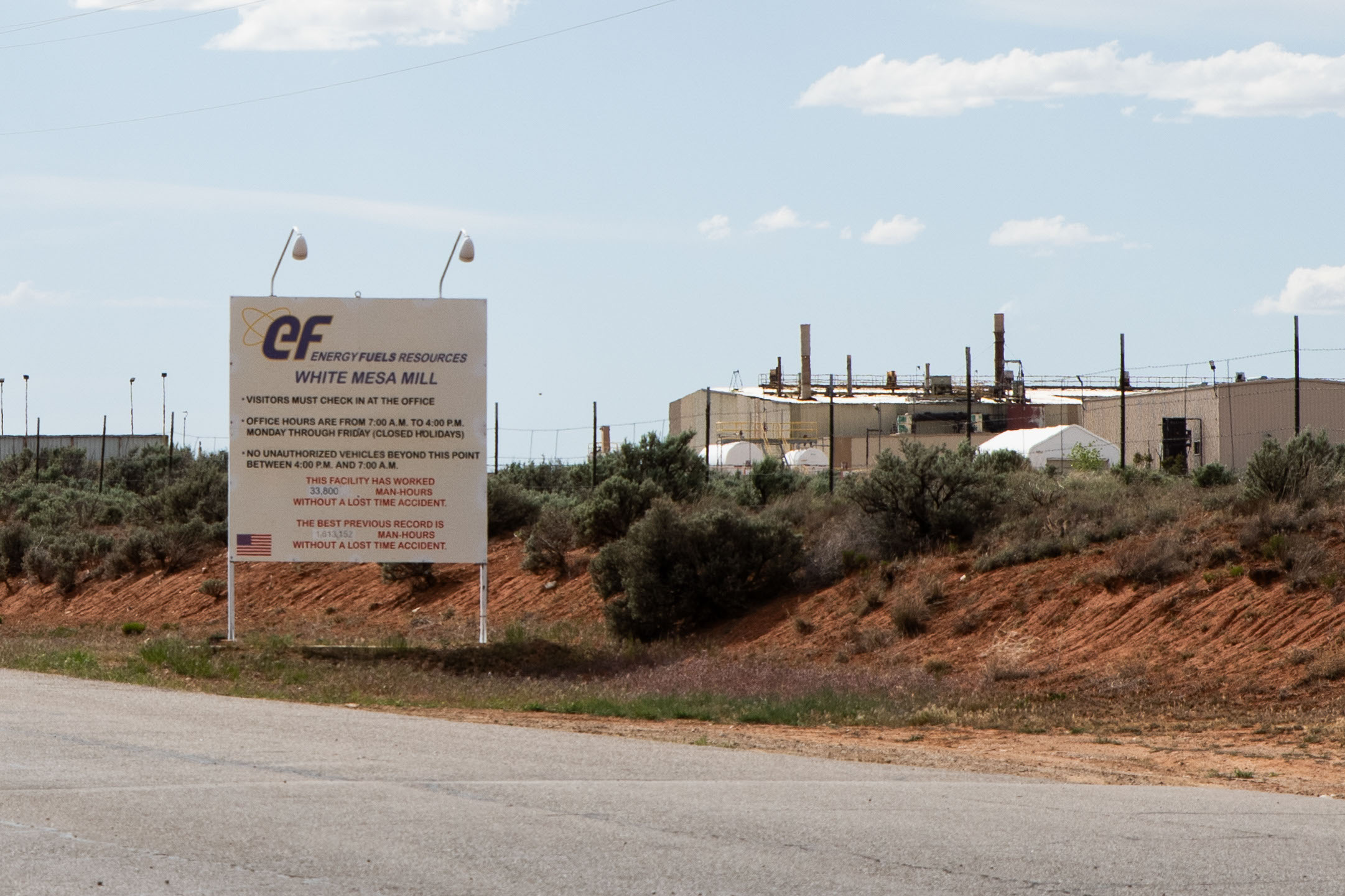 A photo shows a sign in front of White Mesa Mill. The facility is seen in the background.