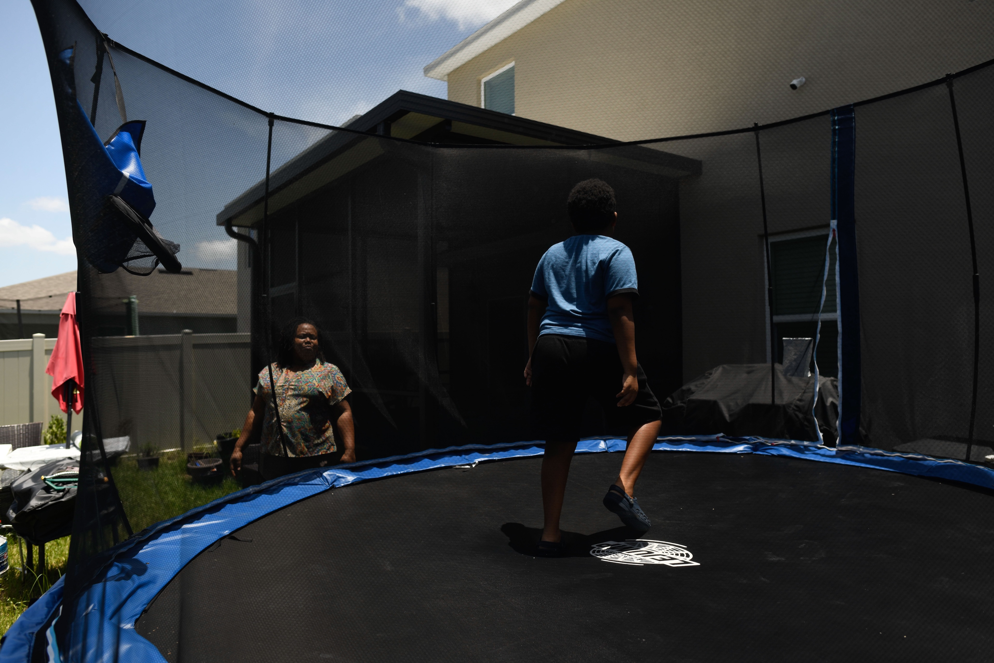 A young boy jumps on a trampoline while his mother watches