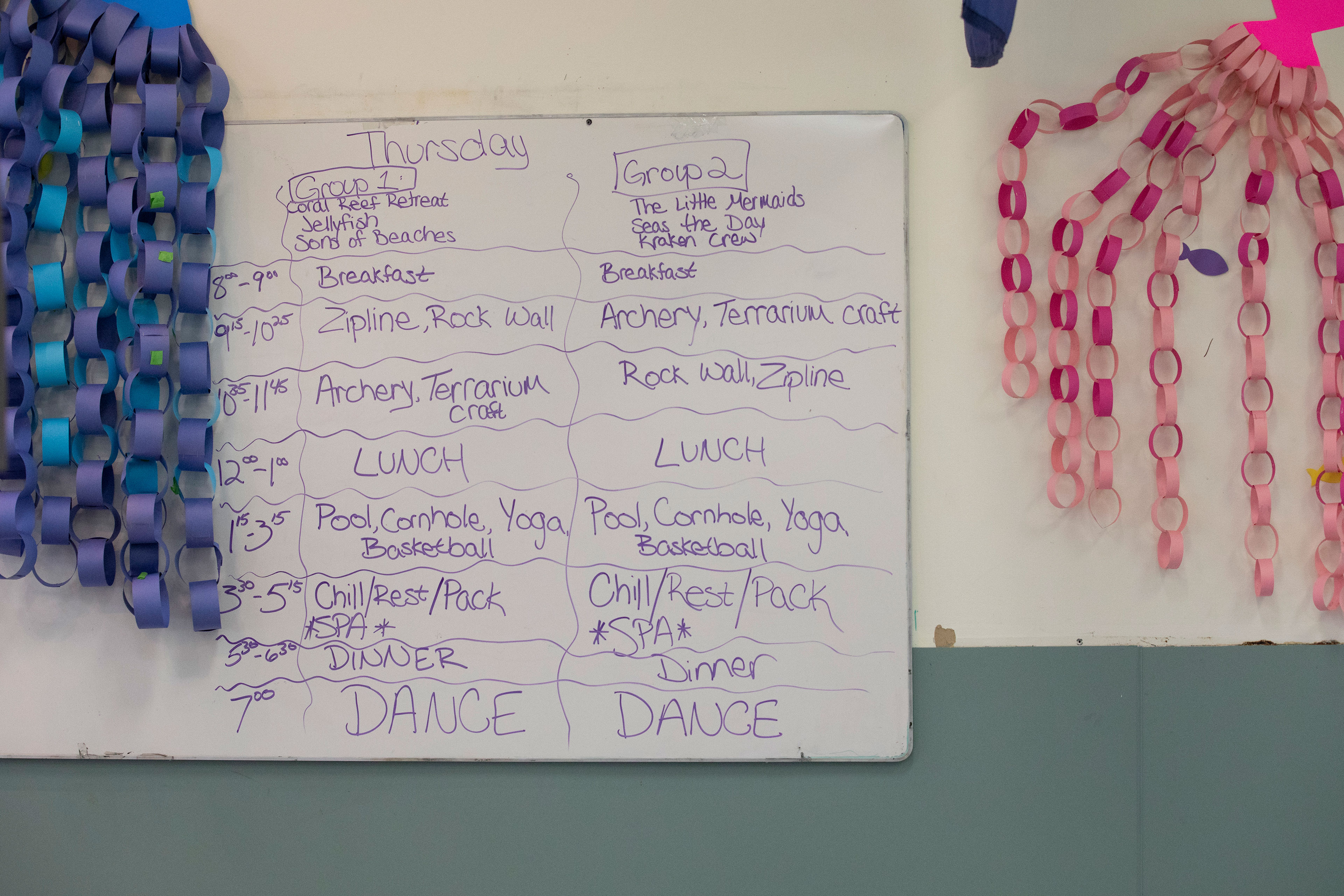 A whiteboard on a wall with "Thursday" written at the top outlines the activities and times for two groups throughout the day.