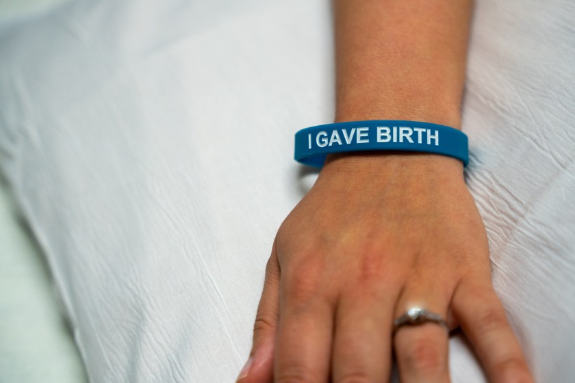 A photo of a woman's hand. She wears a blue wristband that reads, "I gave birth."