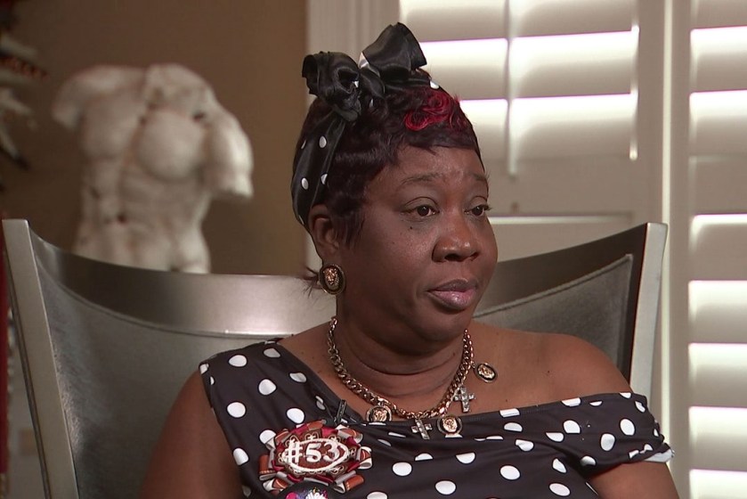 A Black woman sits for a TV interview indoors.
