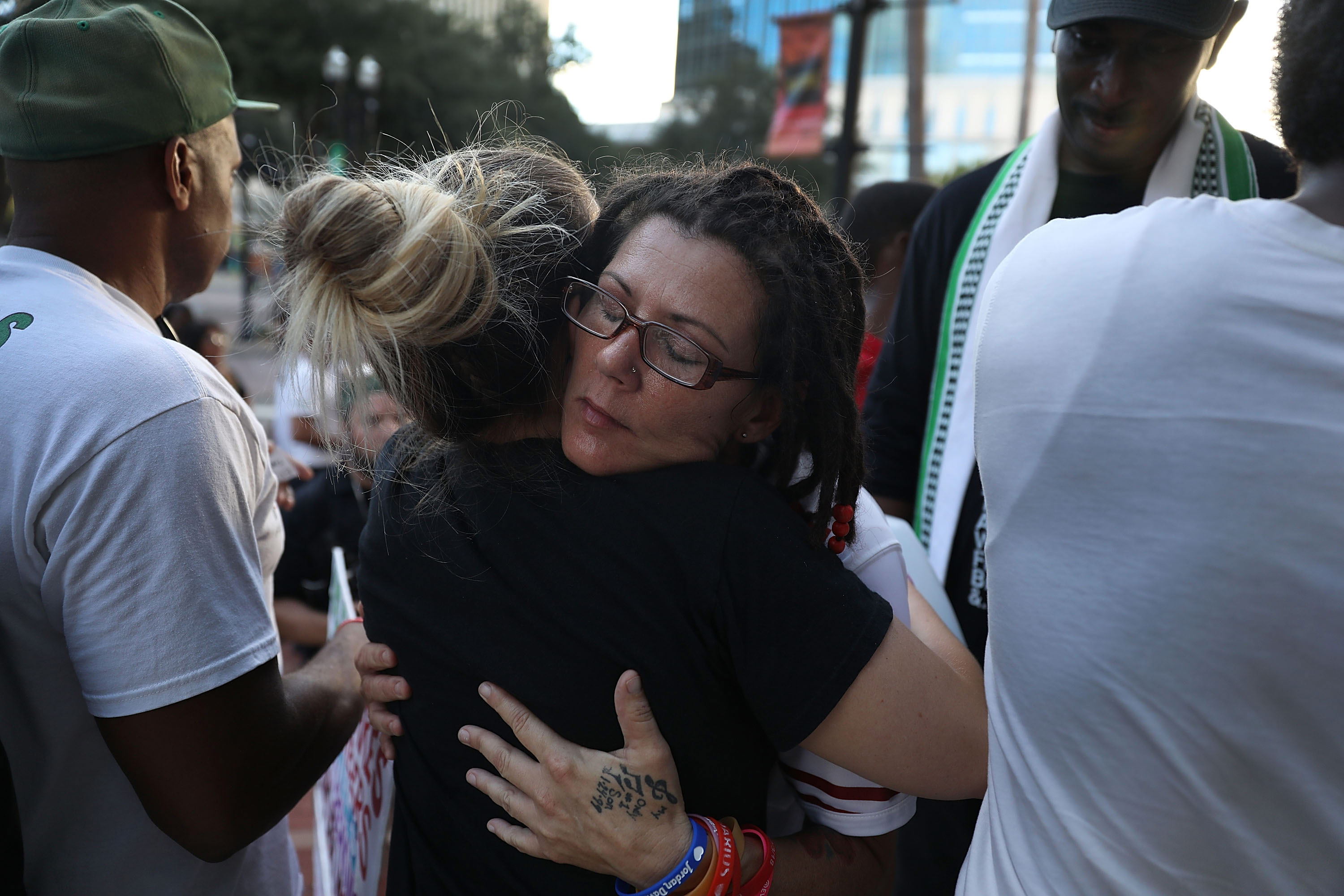 A photo shows a white woman being hugged outside in the evening at a gathering.