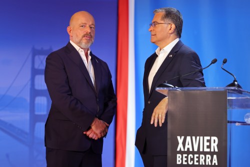 A photo of two men at a televised debate speak to one another on stage.