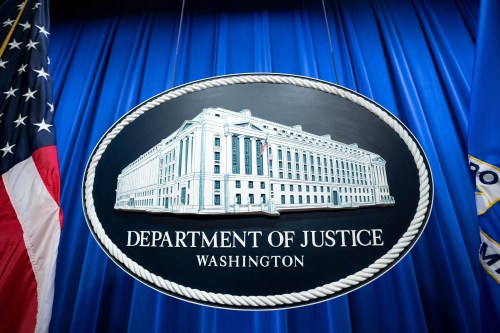 Department of Justice signage hangs in front of a blue curtain.