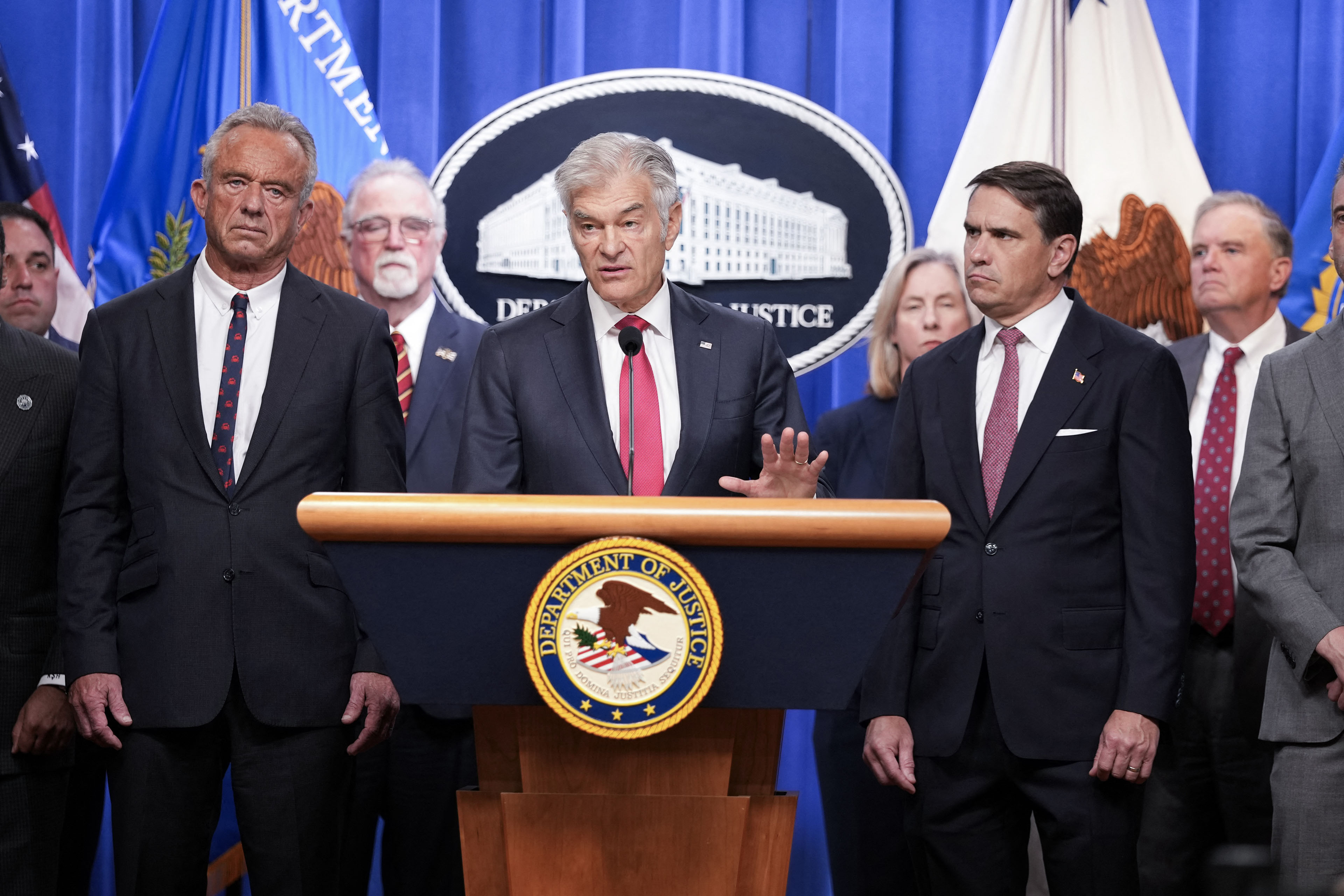 Mehmet Oz (center) flanked by Acting Attorney General Todd Blanche (right) and US Secretary of Health and Human Services Robert F. Kennedy Jr. (left), speaks at a podium.