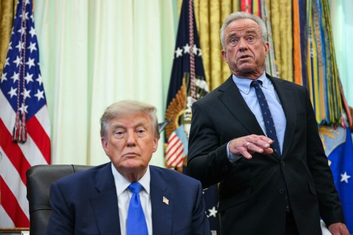 A photo of Donald Trump seated at a desk as Robert F. Kennedy Jr. speaks. They are in the Oval Office.