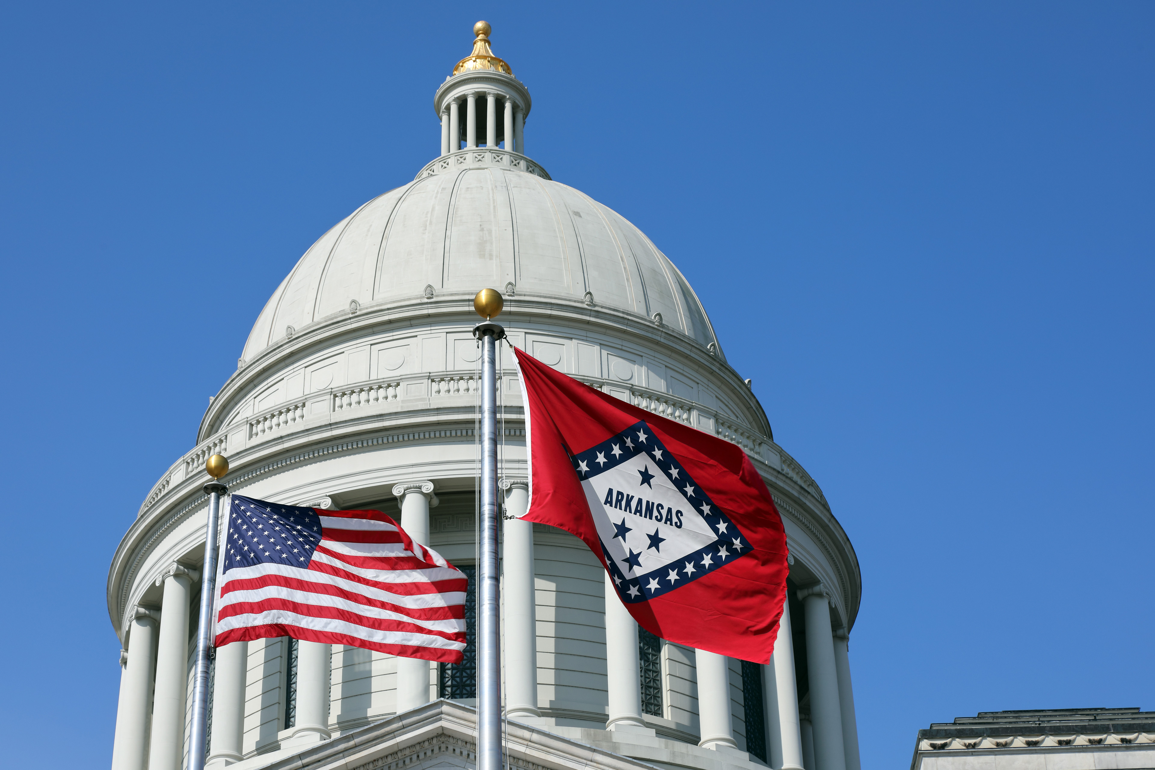 A photo of the rotunda of the Arkansas Capitol. In the foreground on poles are the flags of the United States and Arkansas.