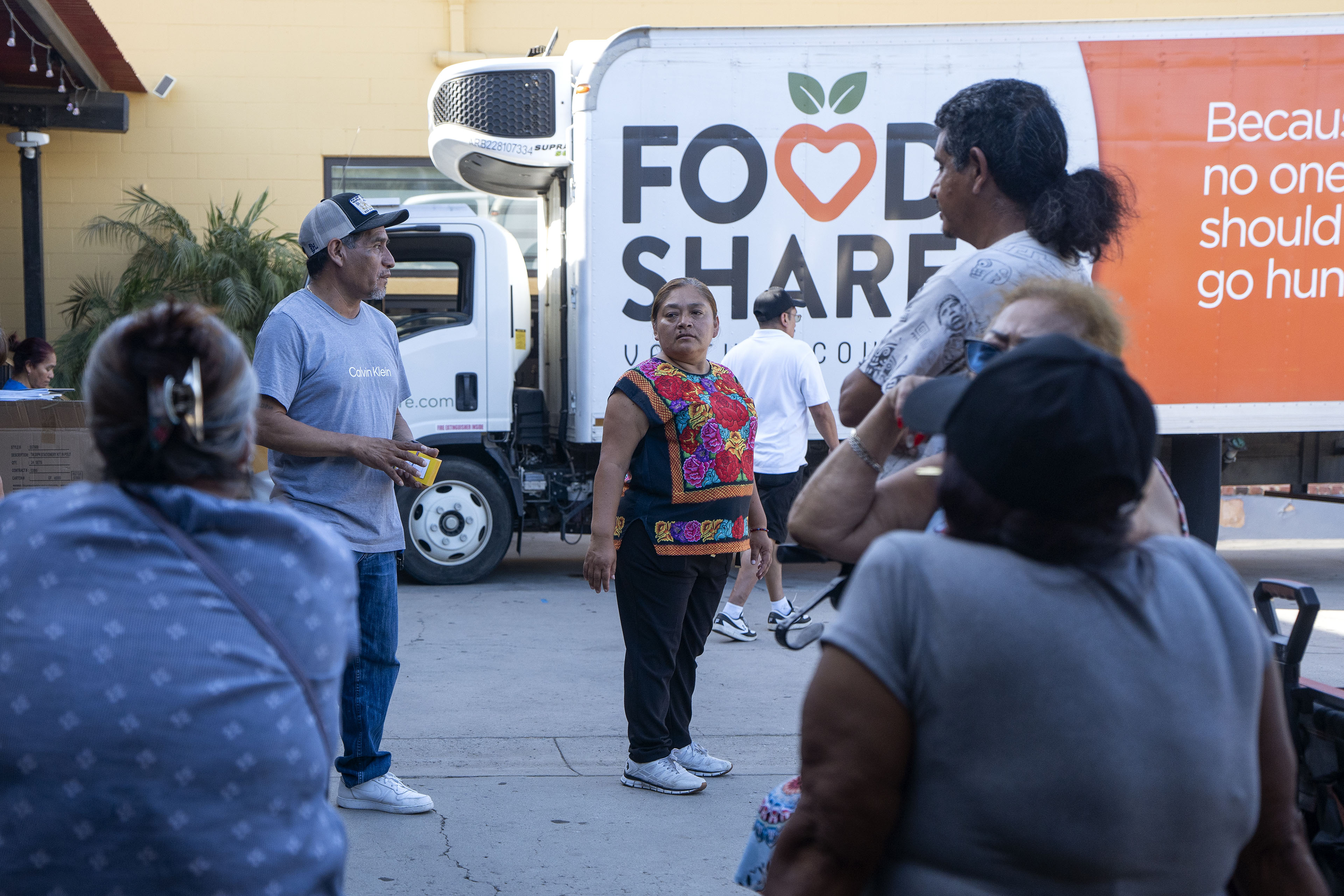A small crowd of people stand in front of a refrigerated delivery truck that says, "Food Share" on the side.