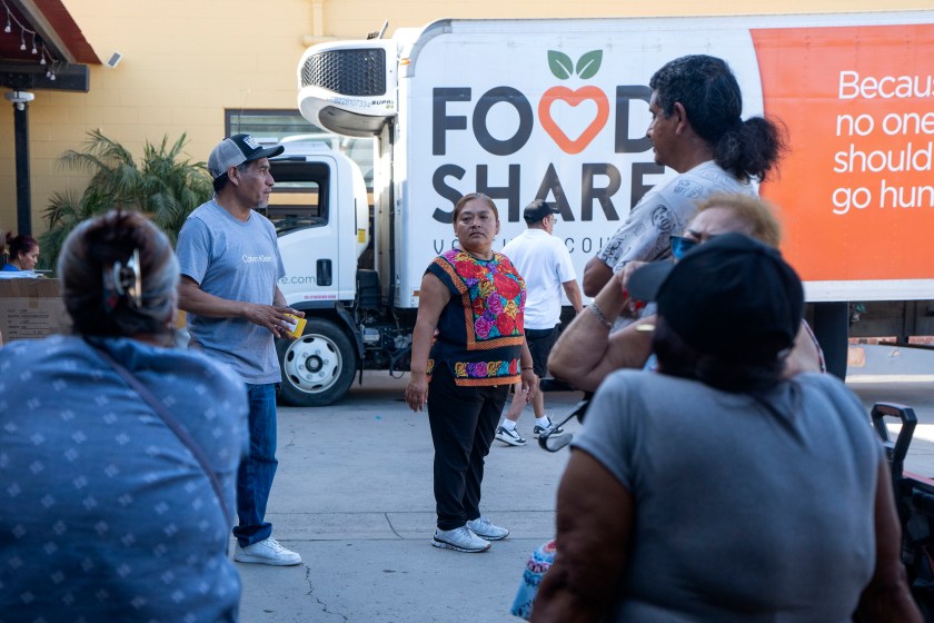 A small crowd of people stand in front of a refrigerated delivery truck that says, "Food Share" on the side.