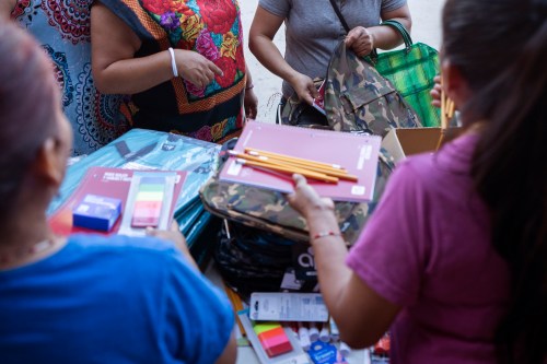 People stand around children's school supplies, handing them out to those who need them.
