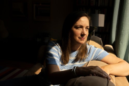 A portrait of a white woman leaning on a couch by a window, casting dramatic lighting across her face.