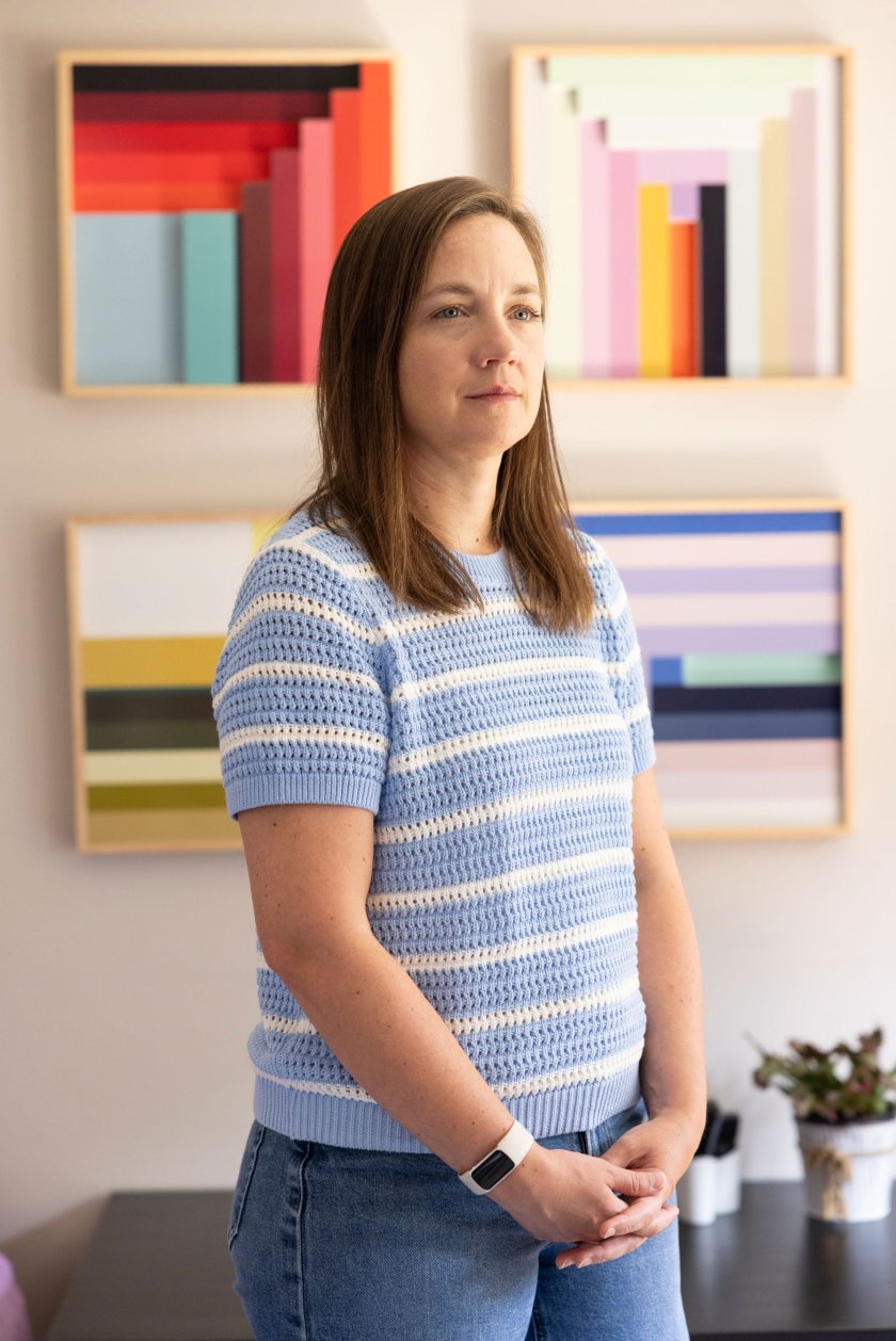 A photo of Stephanie Halver standing in her living room. Four colorful prints are seen hanging on the wall behind her.