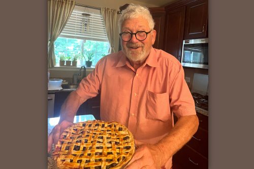 Mike Salmon holds up a lattice-topped blueberry-cinnamon pie, smiling.