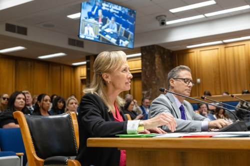 A woman sits at a witness table in a hearing room.
