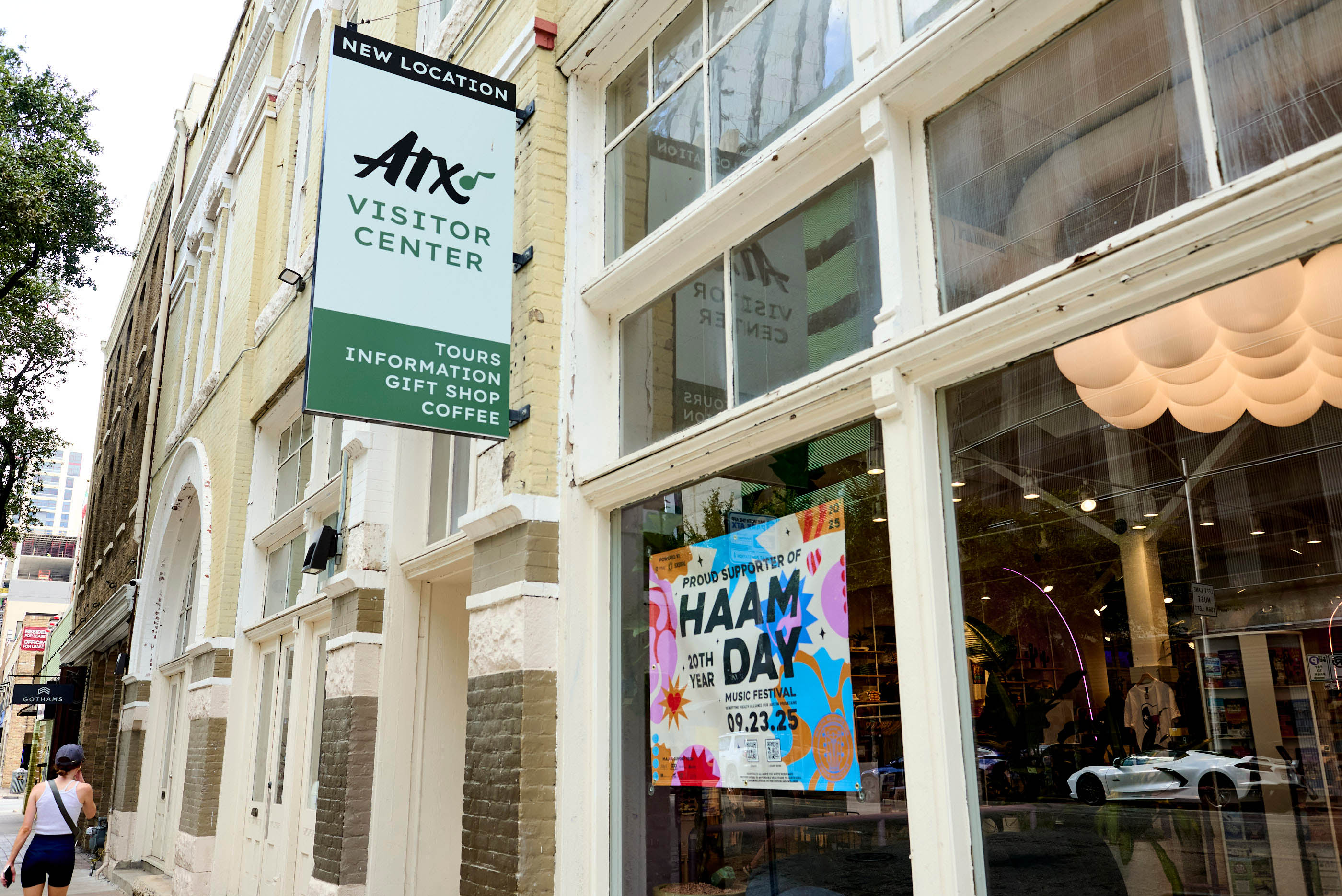 The exterior of a brick building with large windows. In the window is a colorful sign that says,