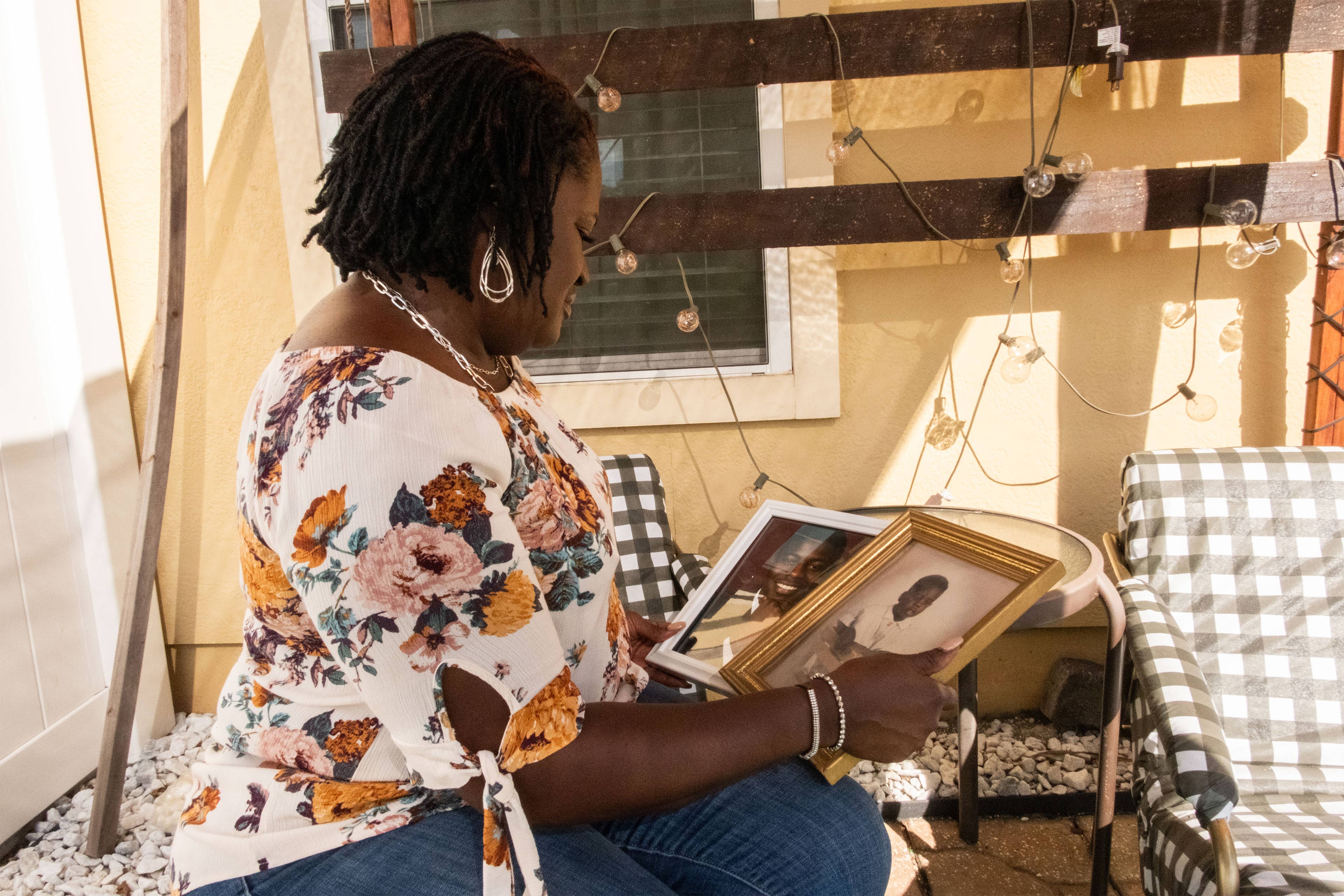 A Black woman sits outside as she holds two framed photos of her son.