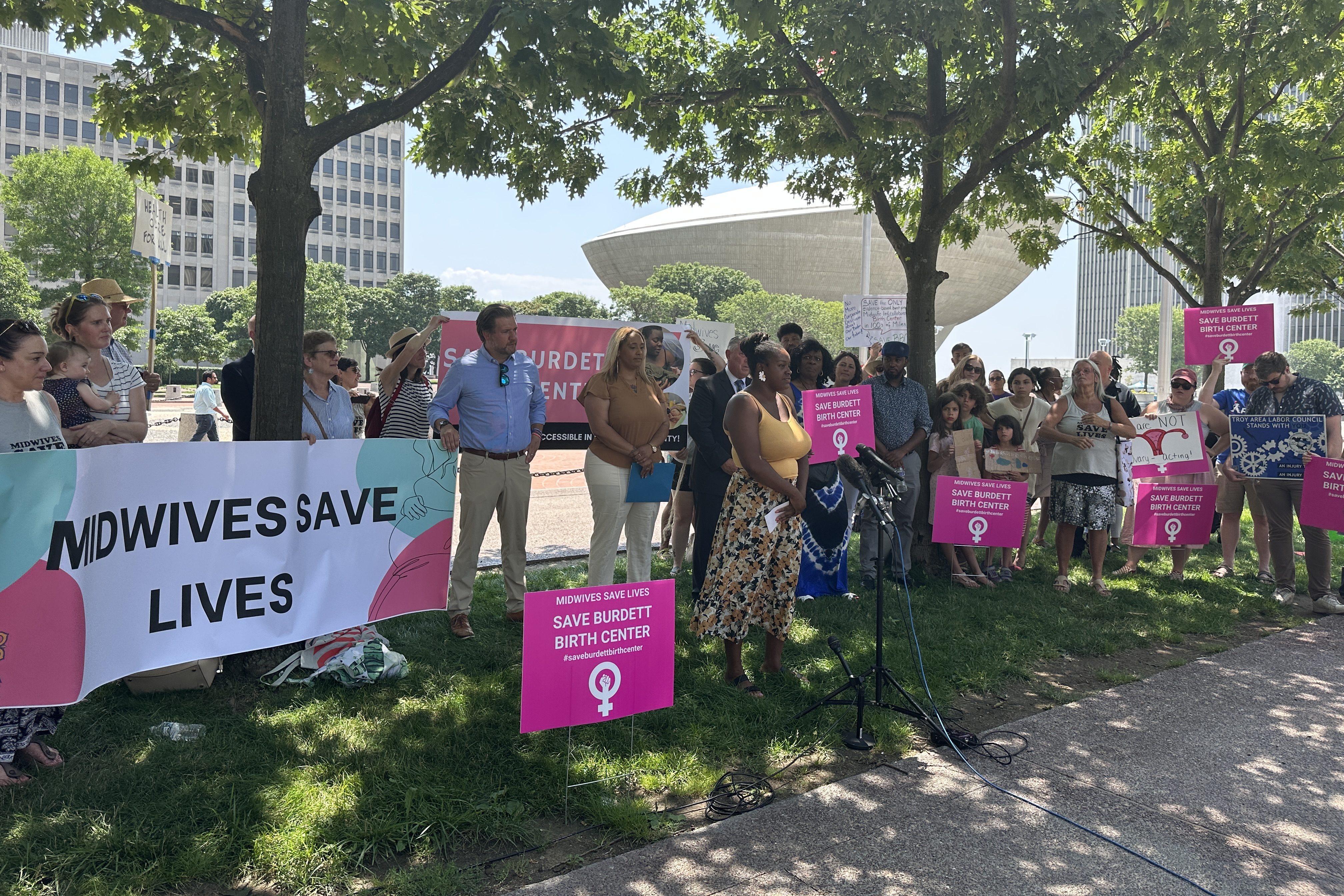 A crowd of people of various genders, ethnicities, and ages stand with signs that say "Save Burdett Birth Center."