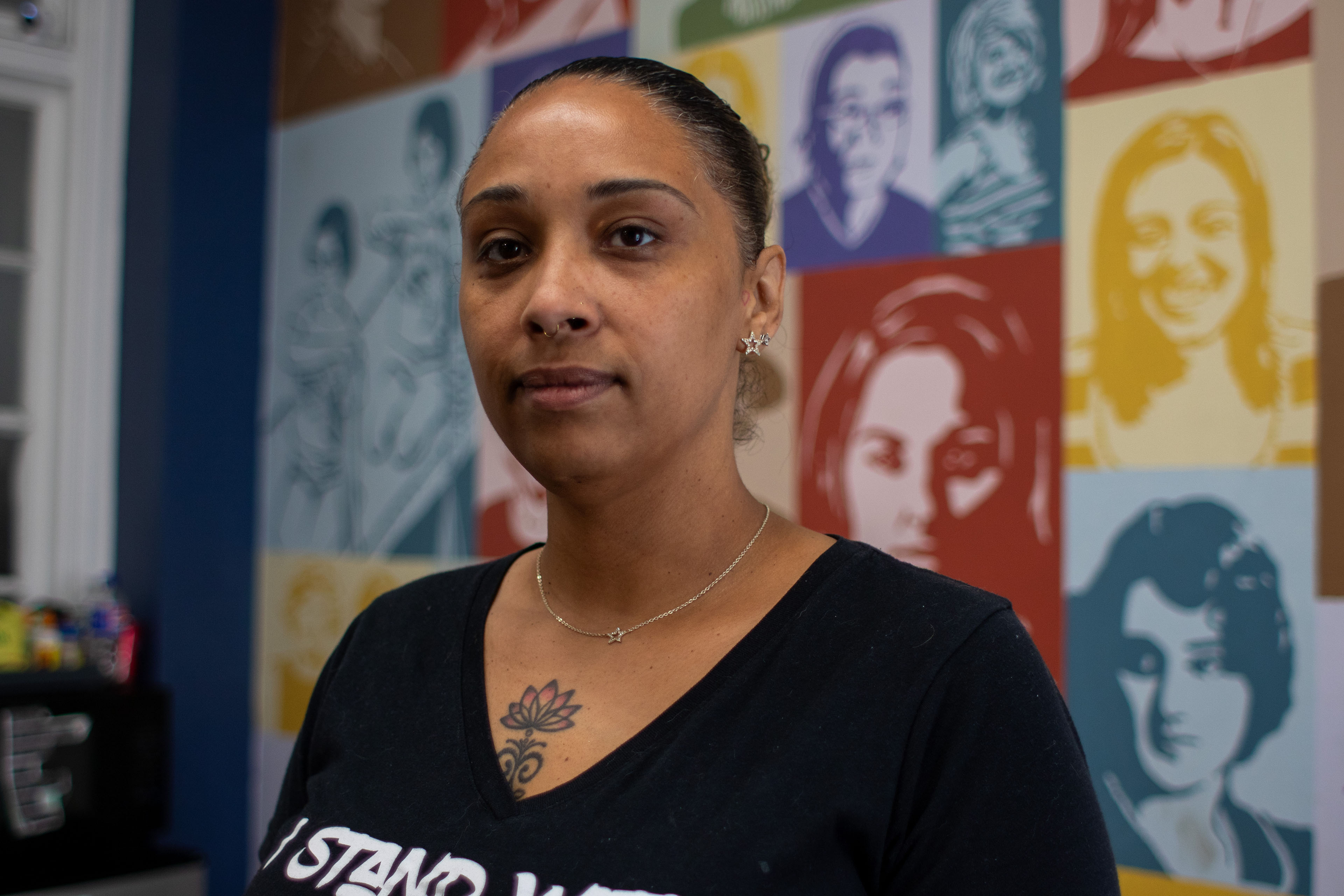 A woman wearing a black T-shirt looks towards the camera. She wears a necklace with a tiny star on it, with earrings to match.