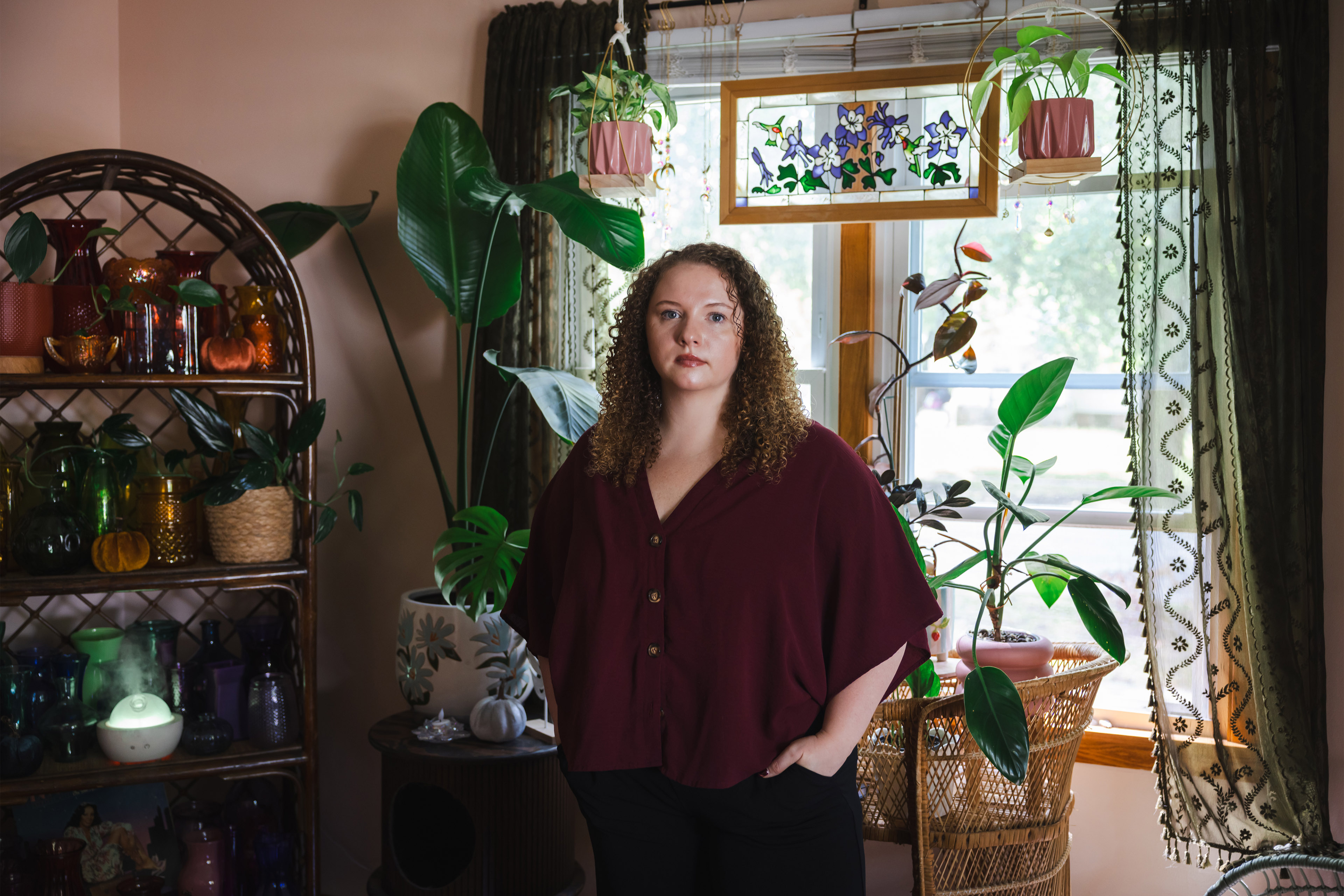 Autumn Daniels stands in front of a window with a variety of plants on shelves.