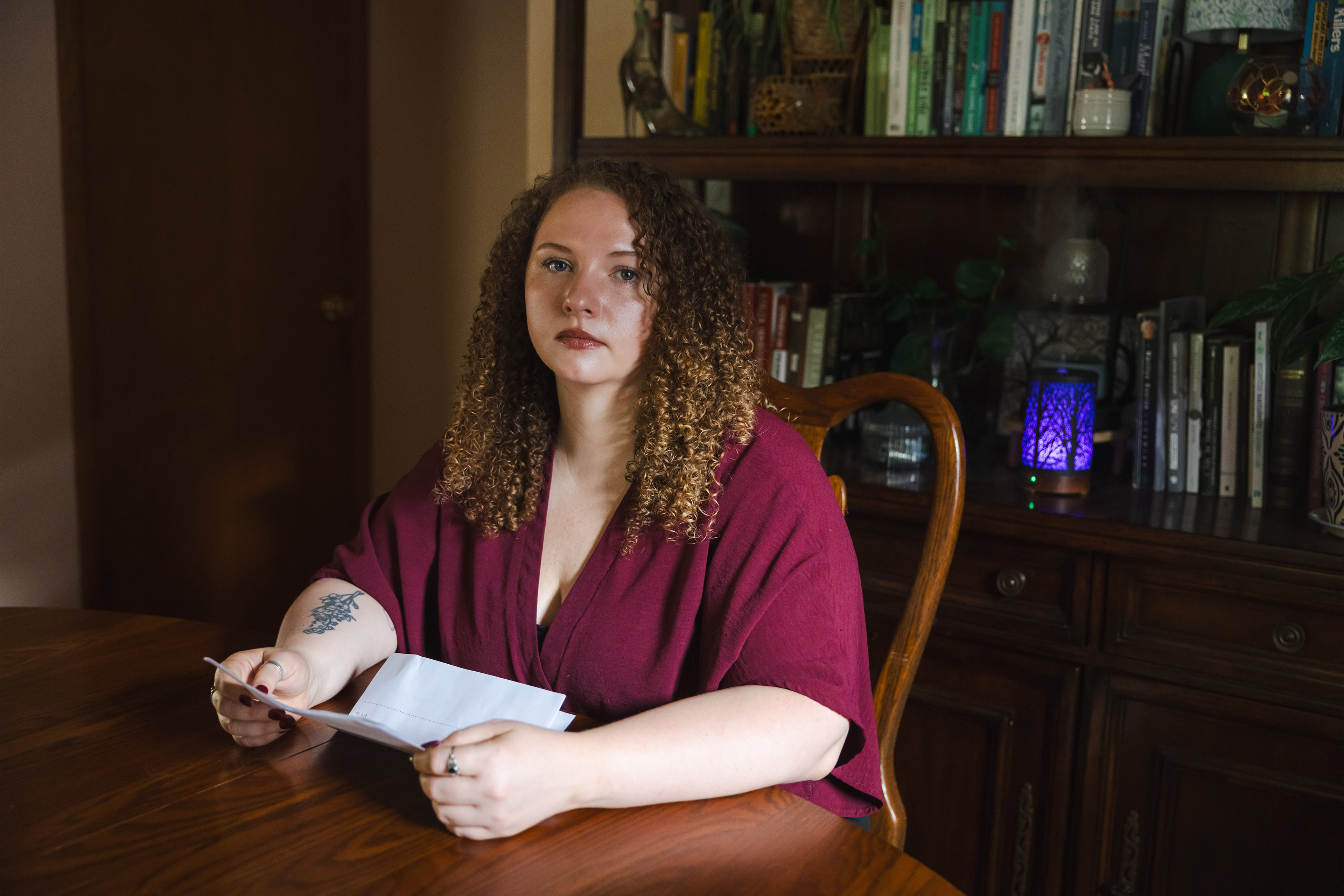 A woman sits at a table for a portrait, holding a copy of her medical bill.