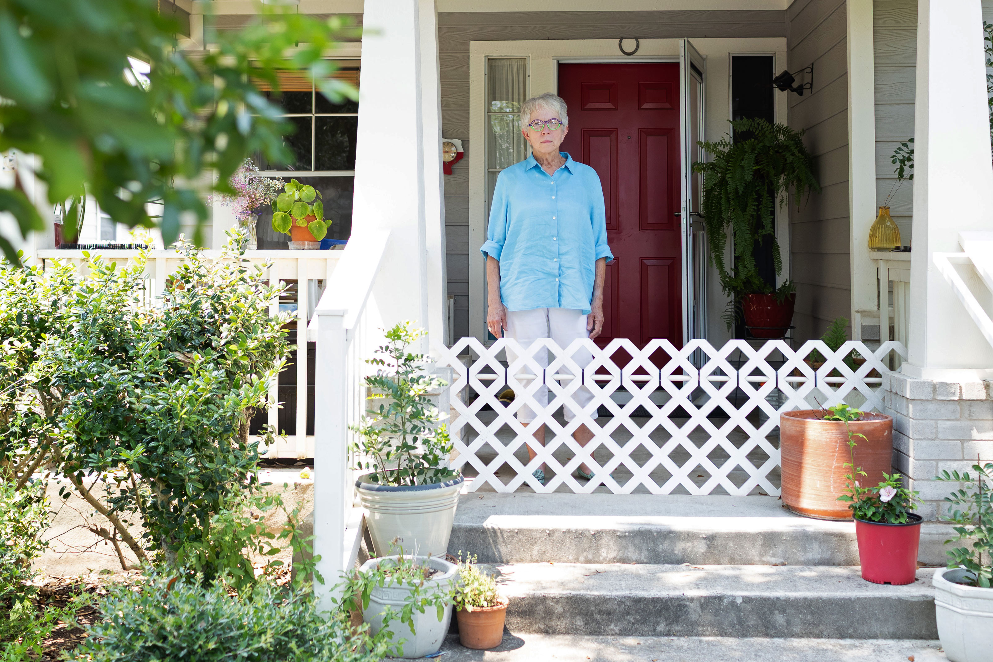 Cindy Blewett stands on her porch in front of her home. Foliage and plants from her garden on seen to the left.