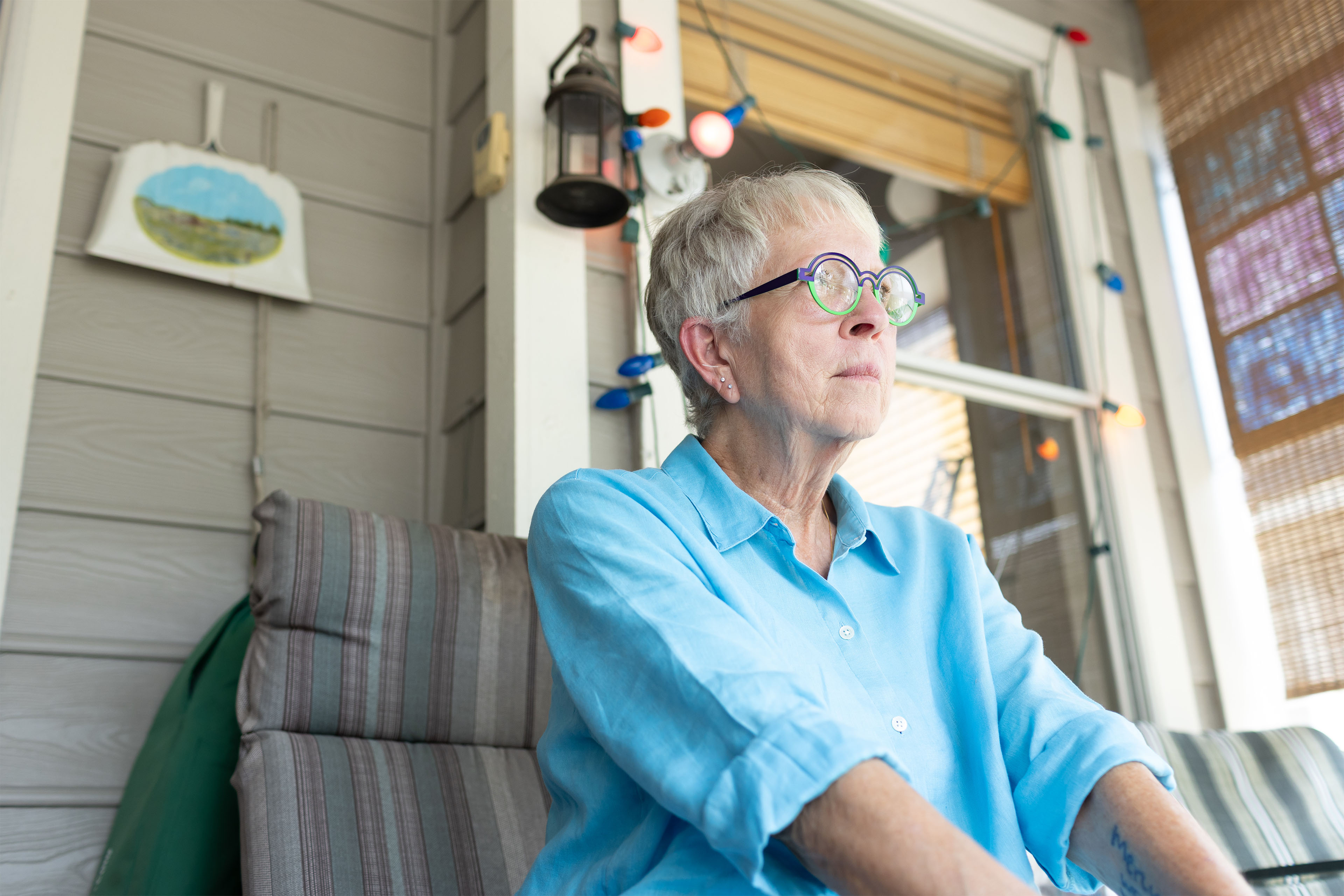 A photo of a woman sitting on a deck outside her home.