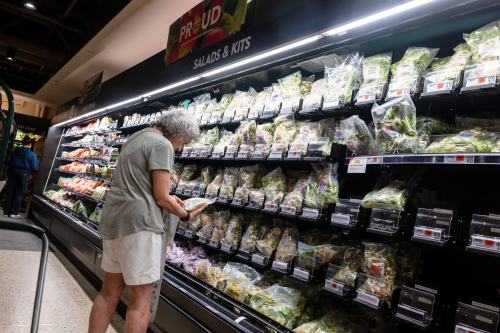 A shopper examines the back of a bagged salad kit at a grocery store.