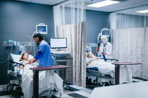A photo of a nurse and doctor treating separate patients divided by curtains in an emergency room.