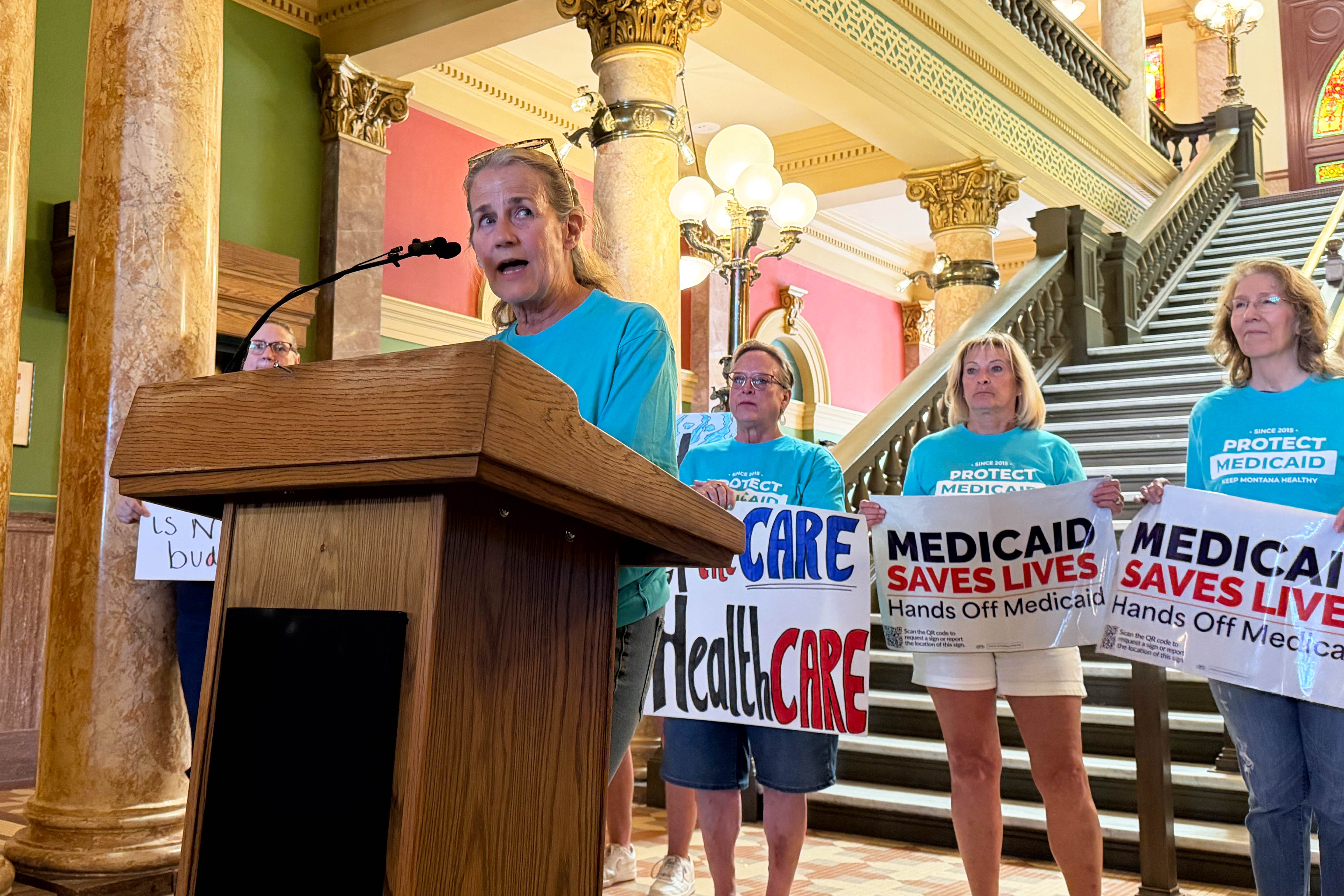 A photo of Rep. Mary Caferro speaking at a podium. Behind her stand several women holding signs that read, "Keep the care in healthcare," and "Medicaid saves lives. Hands off Medicaid."