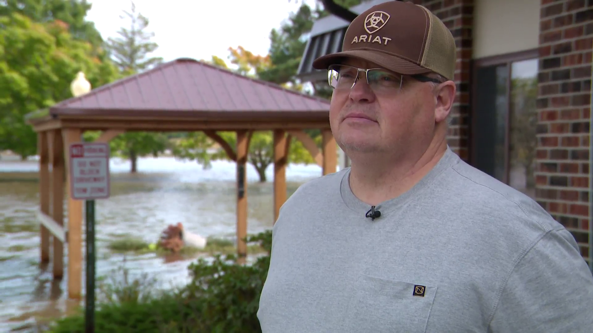 A man stands in front of a building and the area next to the building behind him is flooded with water.