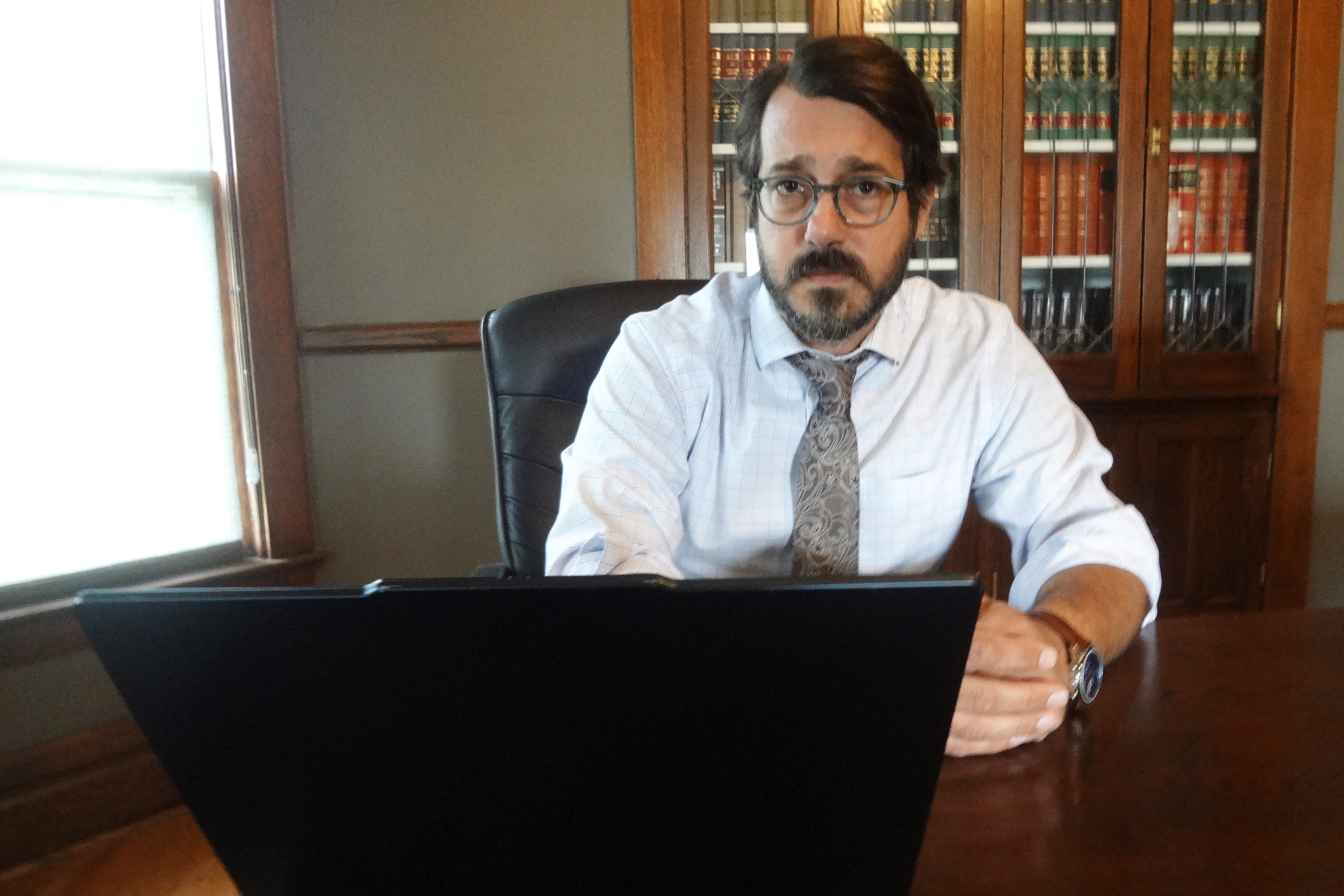 A photo of Sam Petsonk seated at a table indoors. A laptop sits on the table in front of him.