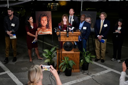 A photo of a group of reporters standing behind a podium at night. Two photos of Christa Pike's victims are seen on stands behind the reporters.