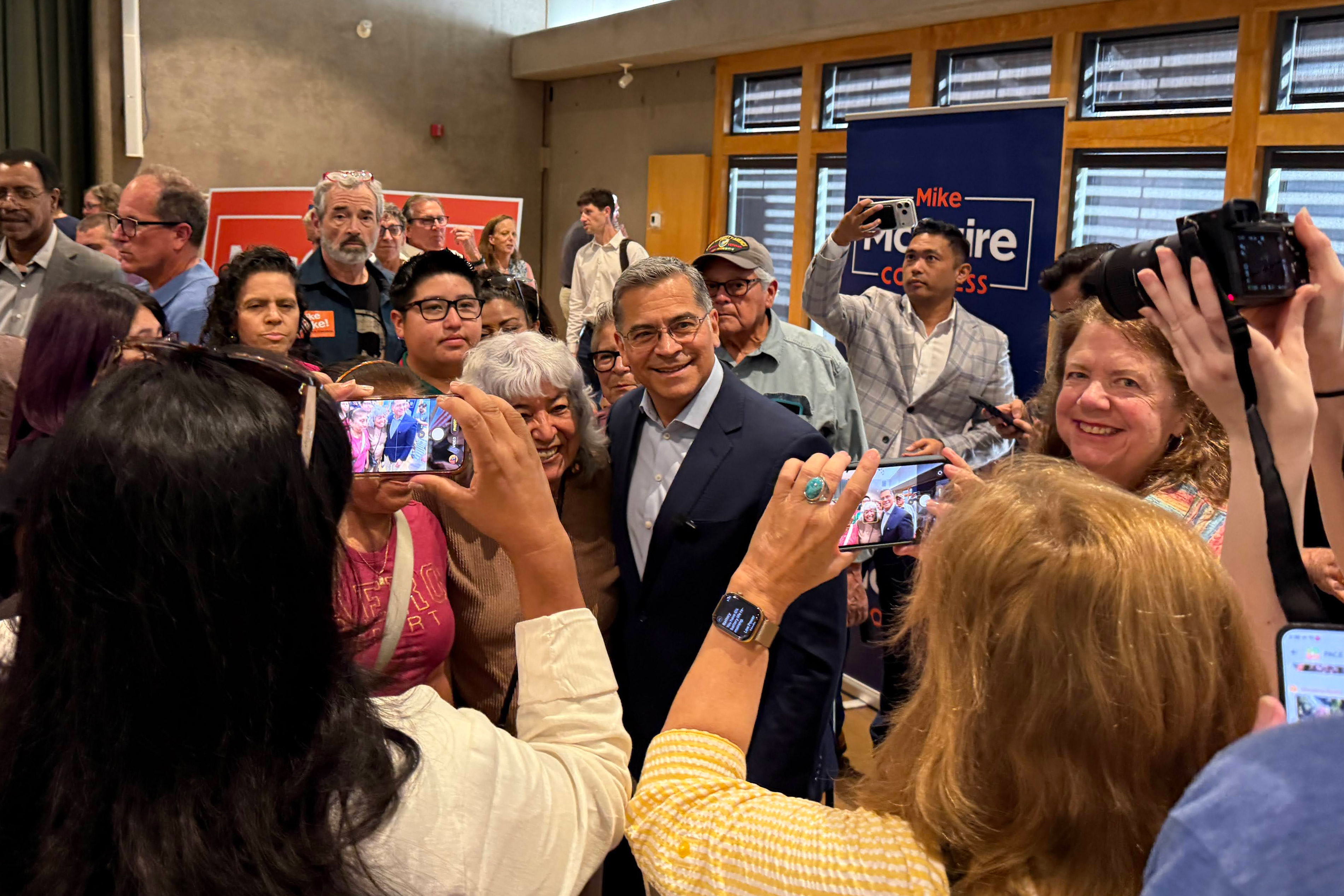A photo of a crowd of people taking pictures of Xavier Becerra at a campaign rally.