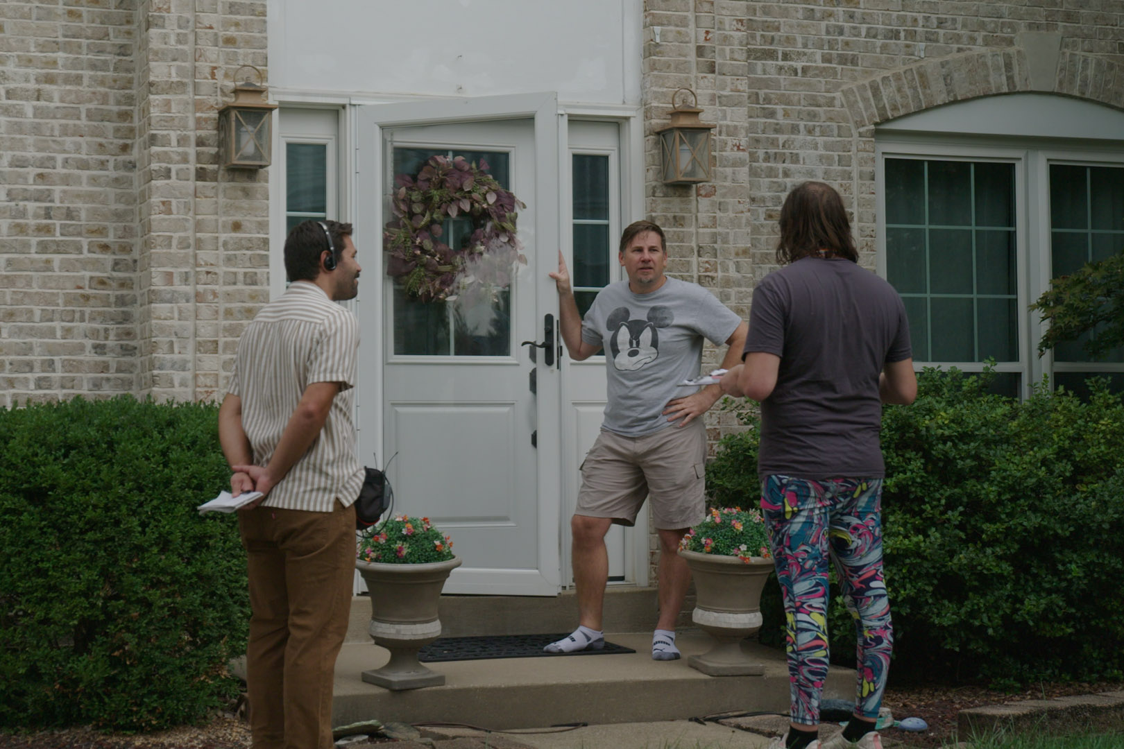 A photo of Reneé Luckfield speaking to a man on his porch. On the left, reporter Bram Sable-Smith observes the conversation.