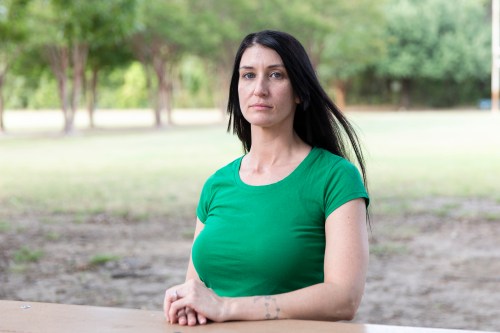 A woman with brown hair, wearing a green shirt, sits at a table in a park