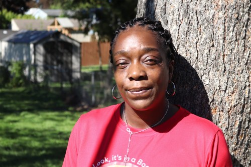 A photo of Christina Starks-Clay standing outside on a sunny day. She is leaning against a tree.