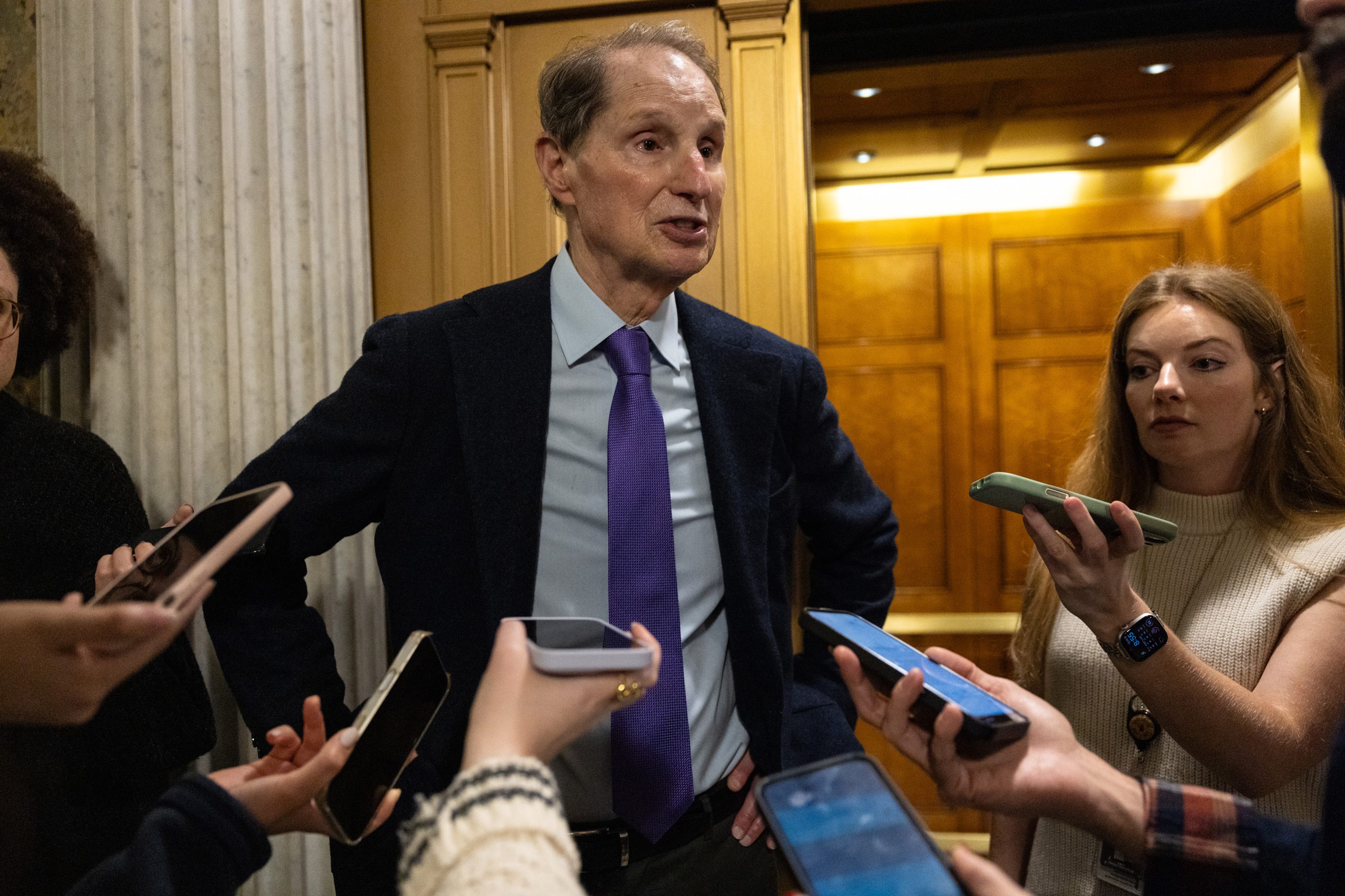 Sen. Ron Wyden speaks to a group of reporters holding their phones at him on Capitol Hill.