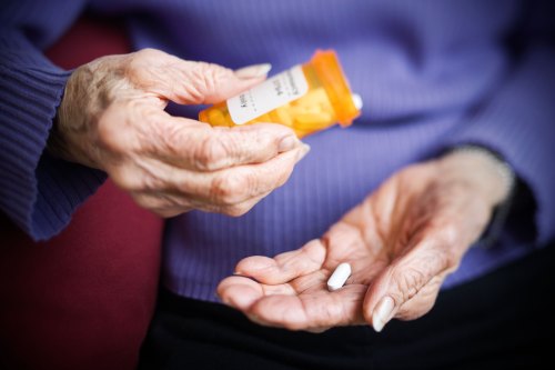A close-up image of wrinkled hands pouring our a pill from an orange bottle into the other hand.