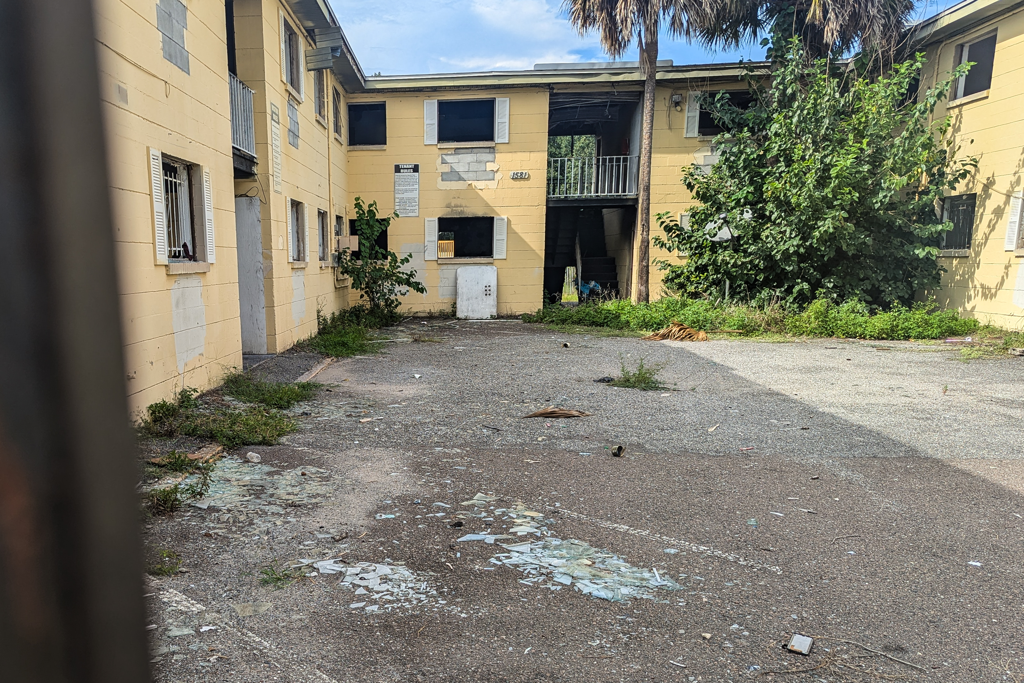 A photo of a courtyard in an abandoned apartment complex. Paint is peeling from the walls and litter is scattered across the ground.
