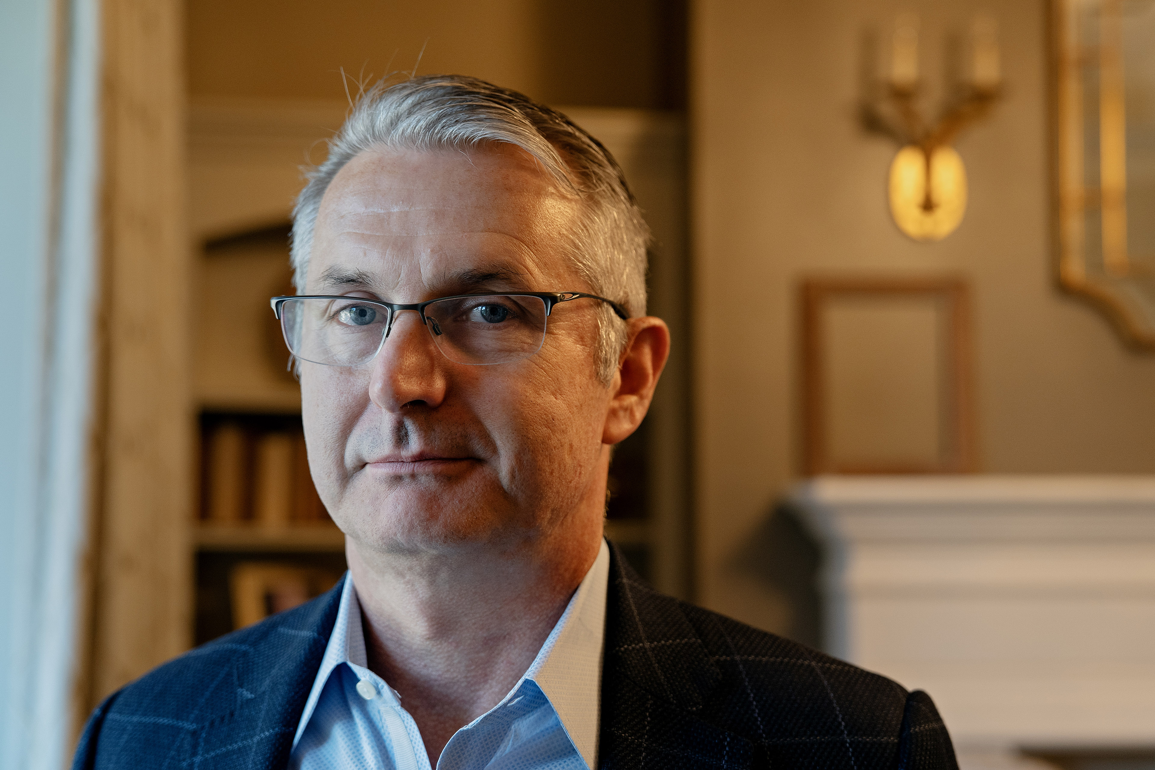 A man with gray hair and glasses looks at the camera while posing for a portrait
