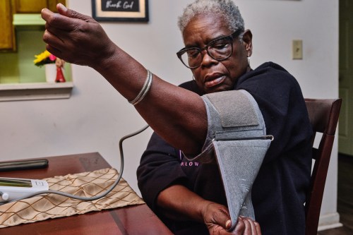 A woman wearing glasses and a black sweatshirt puts a blood pressure cuff on her arm