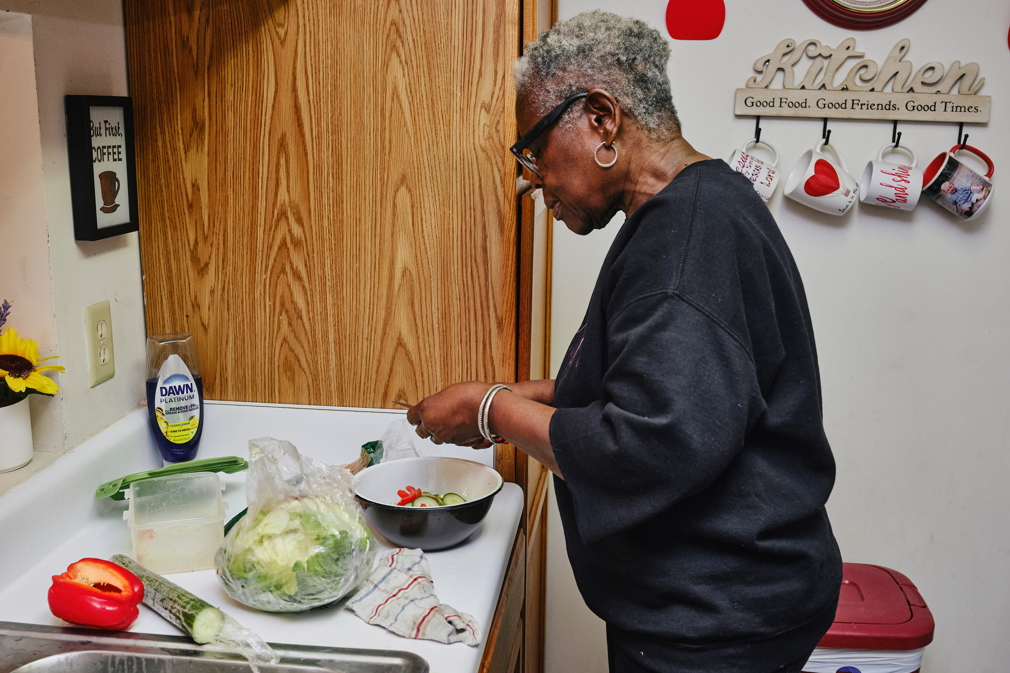 A woman wearing glasses and a black sweatshirt cuts vegetables at a kitchen counter