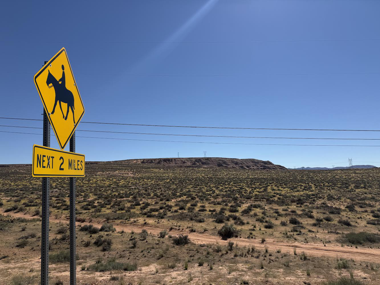 A photo of a vast desert area in Page, Arizona. A yellow street sign warns of equestrian traffic for the next two miles.