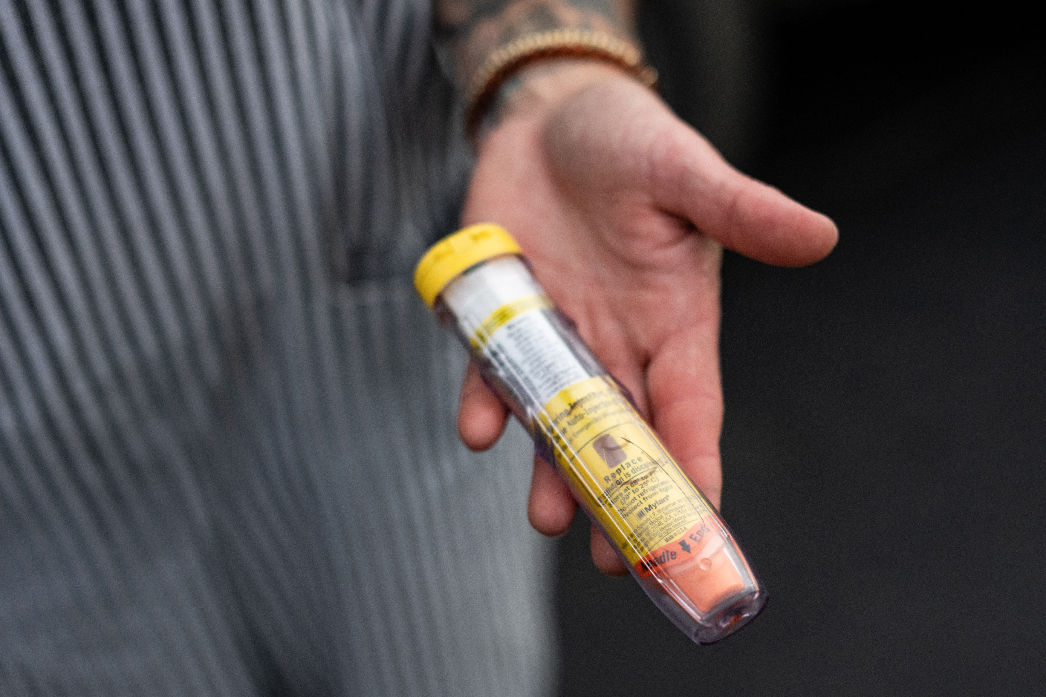 A hand holds an an epinephrine auto-injector for display