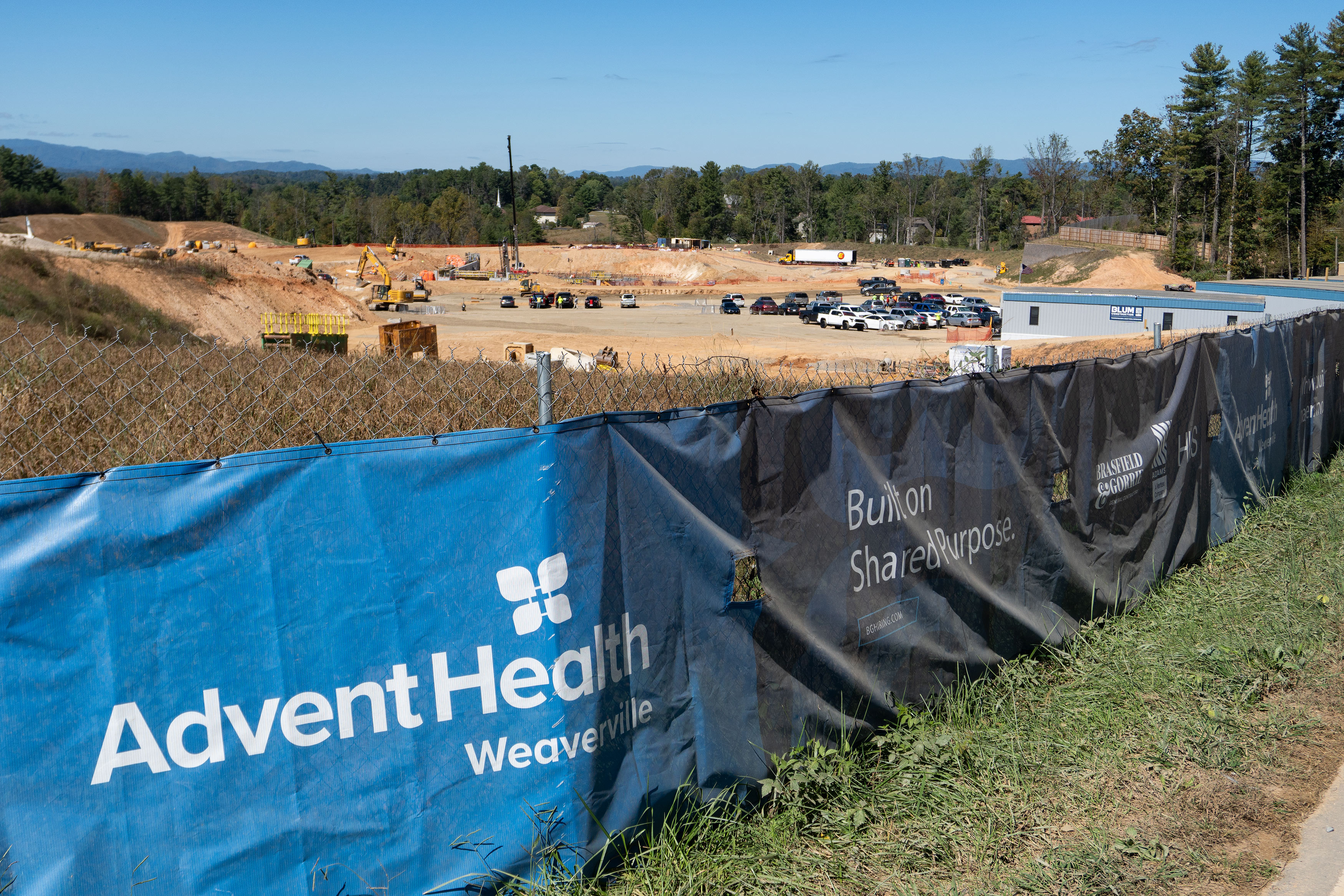 A photo of a construction site. A tarp is draped over the fence surrounding the site. It has AdventHealth Weaverville's logo on it.